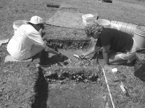 two people kneeling next to shallow excavation pit