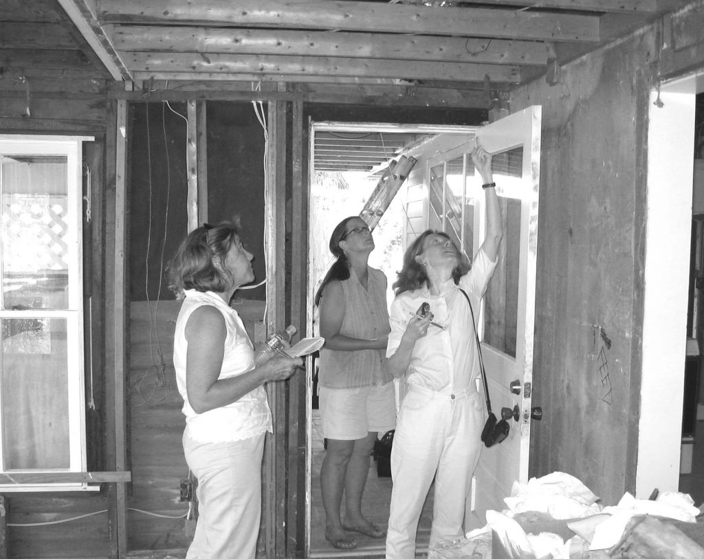 three women look at the ceiling of a house under construction