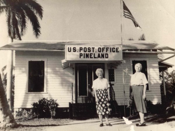 black and white photo of two women standing in-front of a building with the sign US Post Office Pineland
