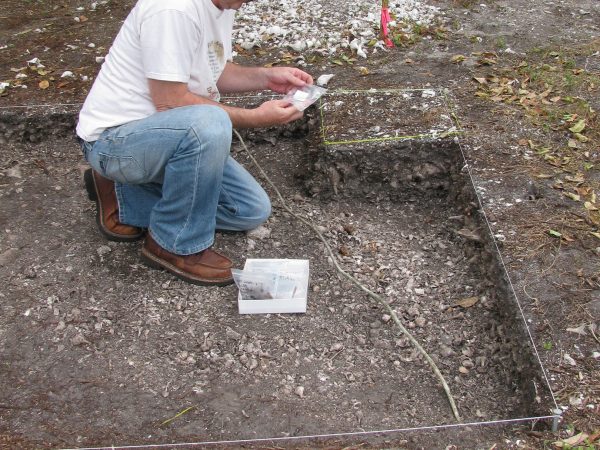 person kneeling in shallow archeological pit