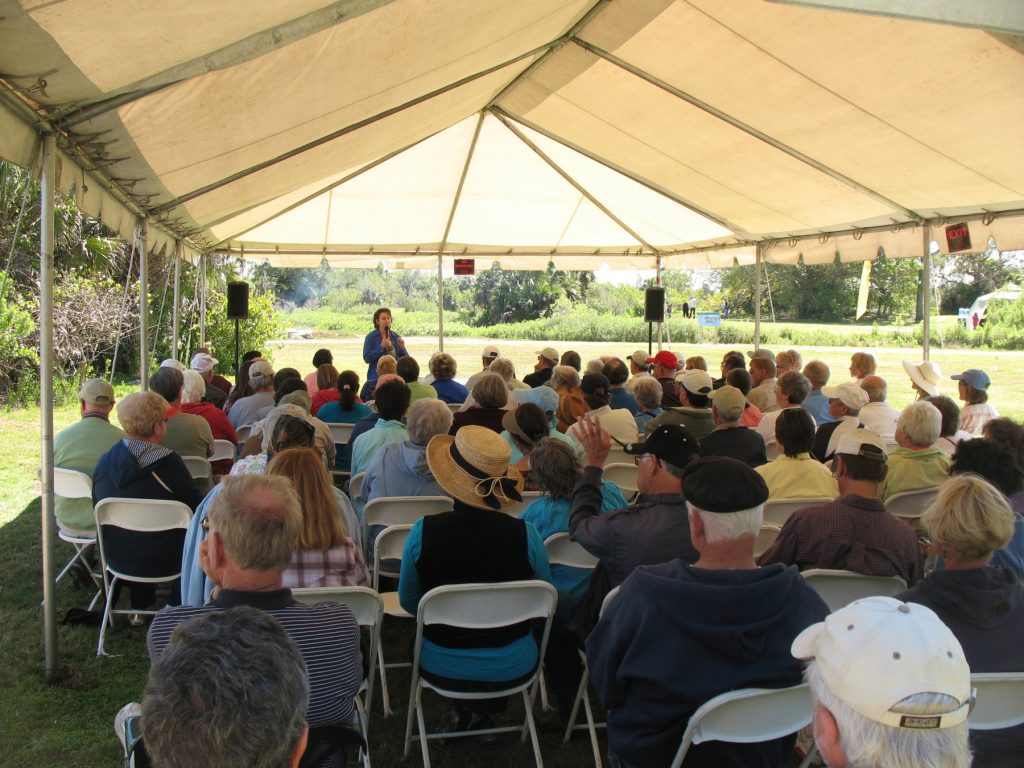 an audience sites under a large tent and listen to a speaker