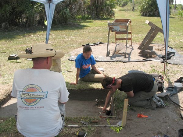 three people sit around an excavation pit