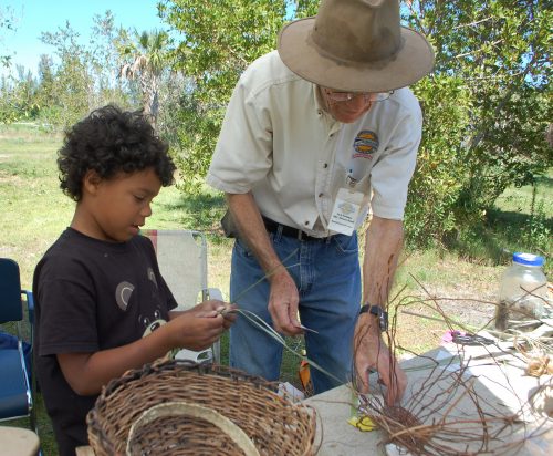 Young child holding basket making items white an adult shows them how to weave a basket