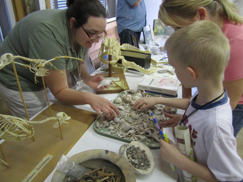 three people leaning over a tray of small bones