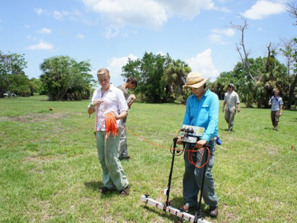 people with survey equipment walk through a field