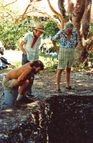 two people standing and one person sitting at the edge of an archaeological excavation pit.