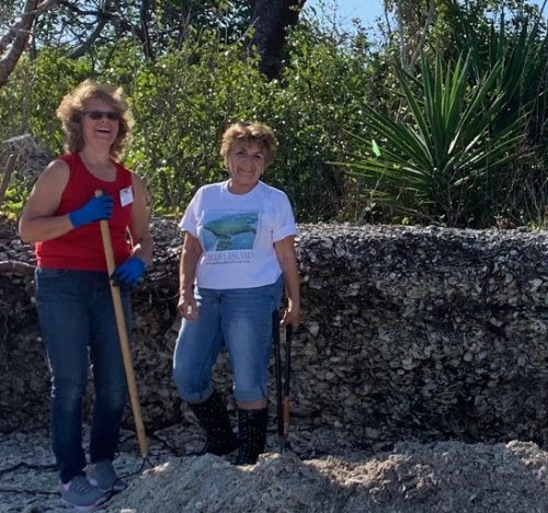 Volunteers Gloria Andrews and Melonnie Hartl stand in front of jagged, eroding North Beach midden.