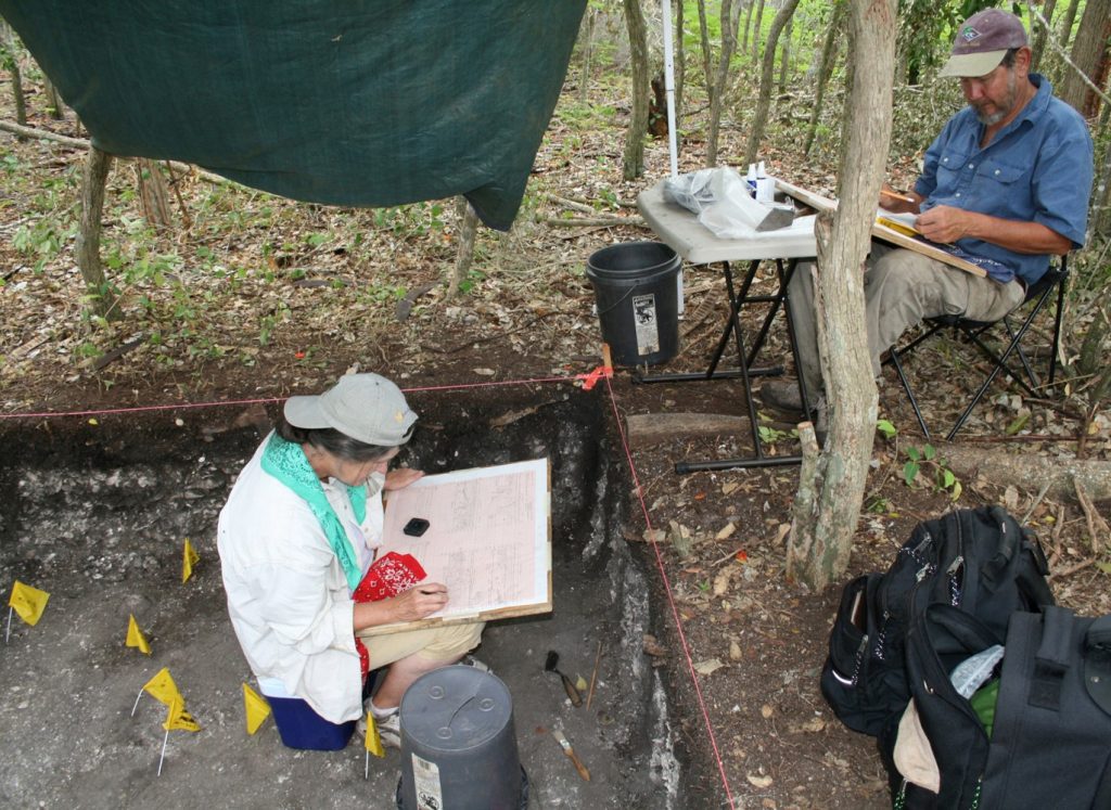two people work on sketch pads at archaeological site