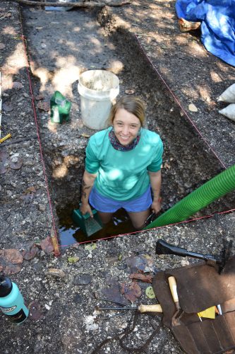 woman stands several feet deep in excavated watercourt berm and underlying oyster midden