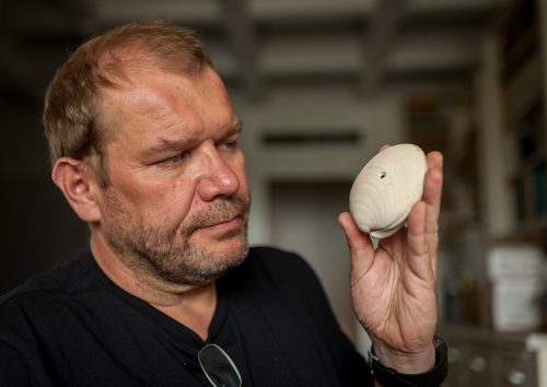 researcher holding a large clam shell with a small hole in the surface