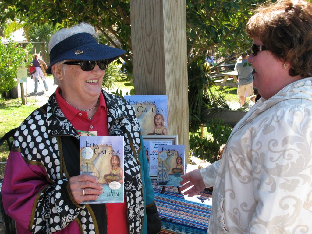 two people stand next to a table with the book "Eye on the Calusa" One person is holding a copy of the book