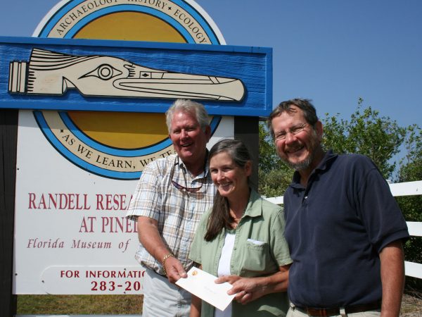 Three people holding a check and standing in front of the Randell Research Center sign