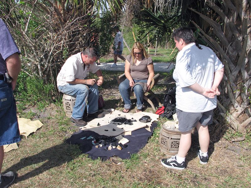 people standing around a blanket with shards of flint. On person demonstrate how to use the flint.