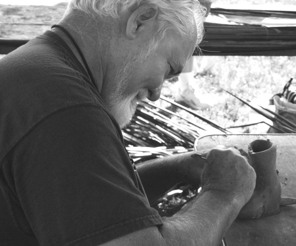 person works on a clay pot