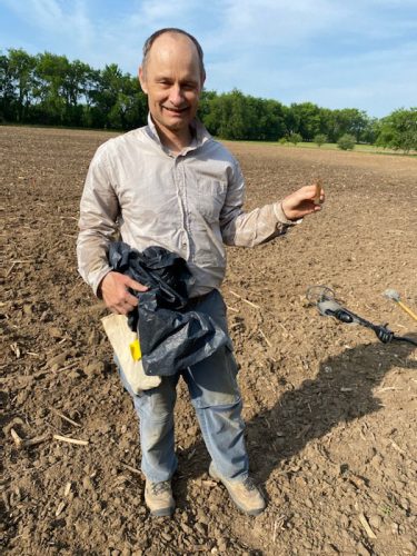 man stands in a field holding a rust-colored piece of metal about the 4” long