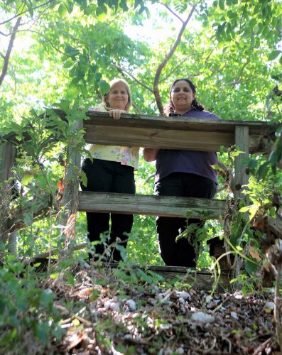 two women stand at a wooden fence.