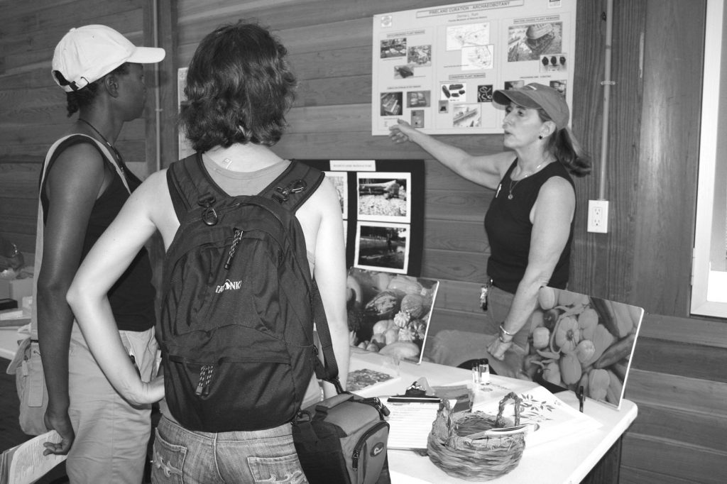 person stands behind table set with photos and speaks with two visitors