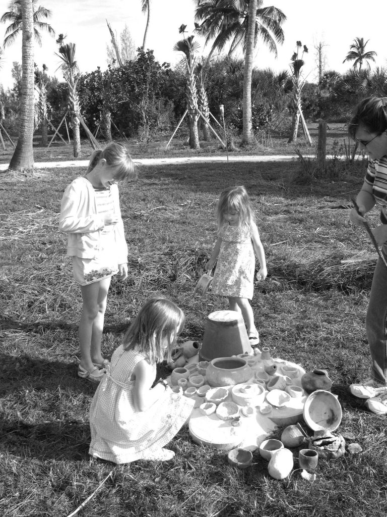 Three young girls stand around a pile of un-fired clay pots