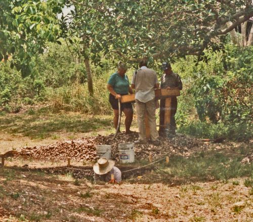 three people stand around a excavation screen while another stands shoulder-deep in the excavation pit