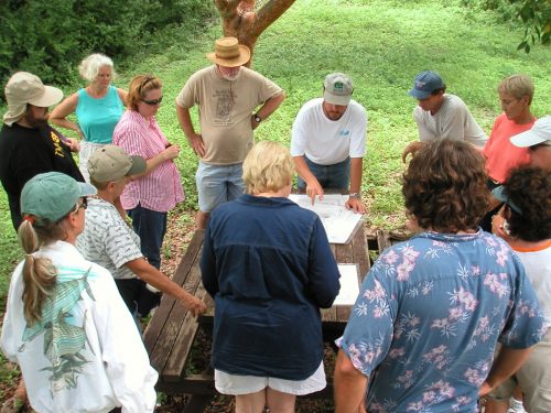 people standing around table listening to researcher 