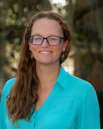 portrait of women with red hair and glasses, wearing a blue shirt