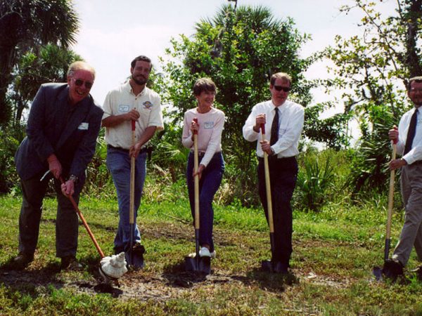 five people standing in a row with shovels for grown breaking ceremony