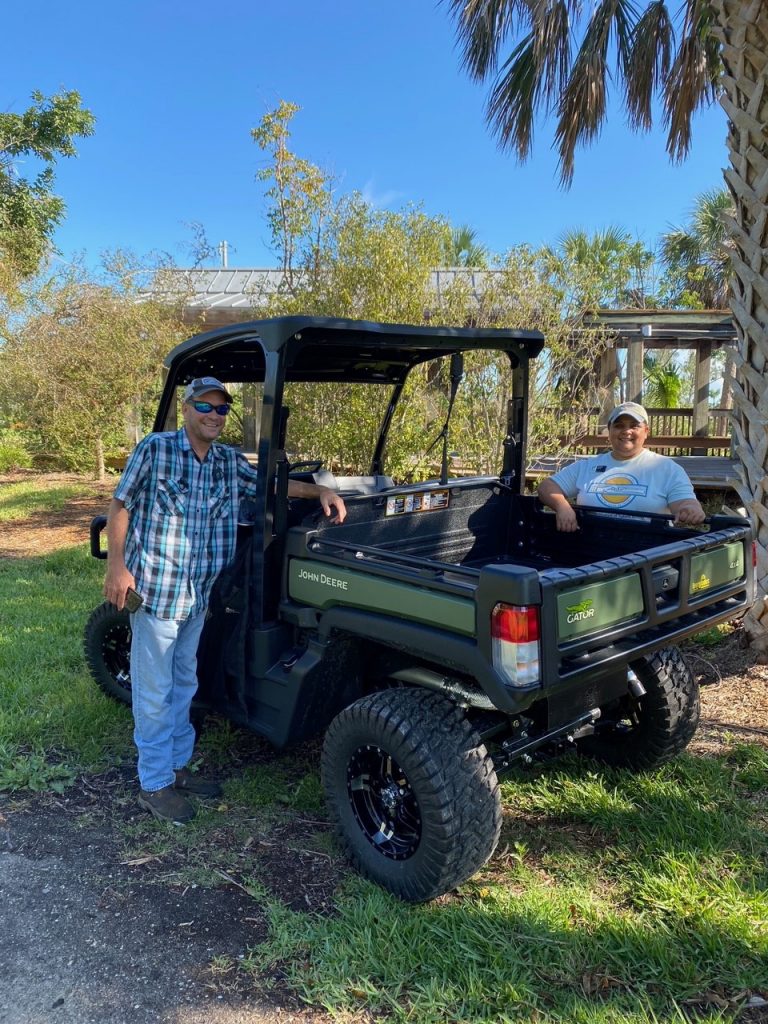 Two people stand next to a John Deere Gator lightweight utility vehicle. They are looking at the camera and smiling