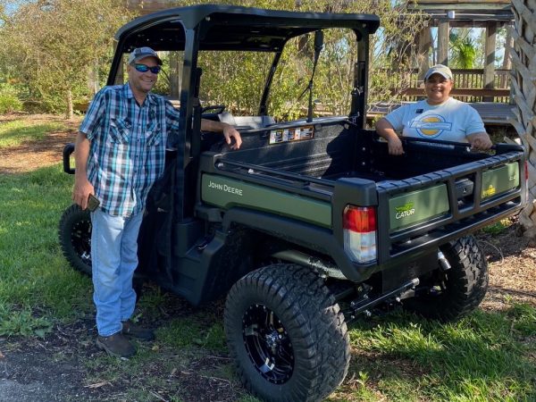 Two people stand next to a John Deere Gator lightweight utility vehicle. They are looking at the camera and smiling