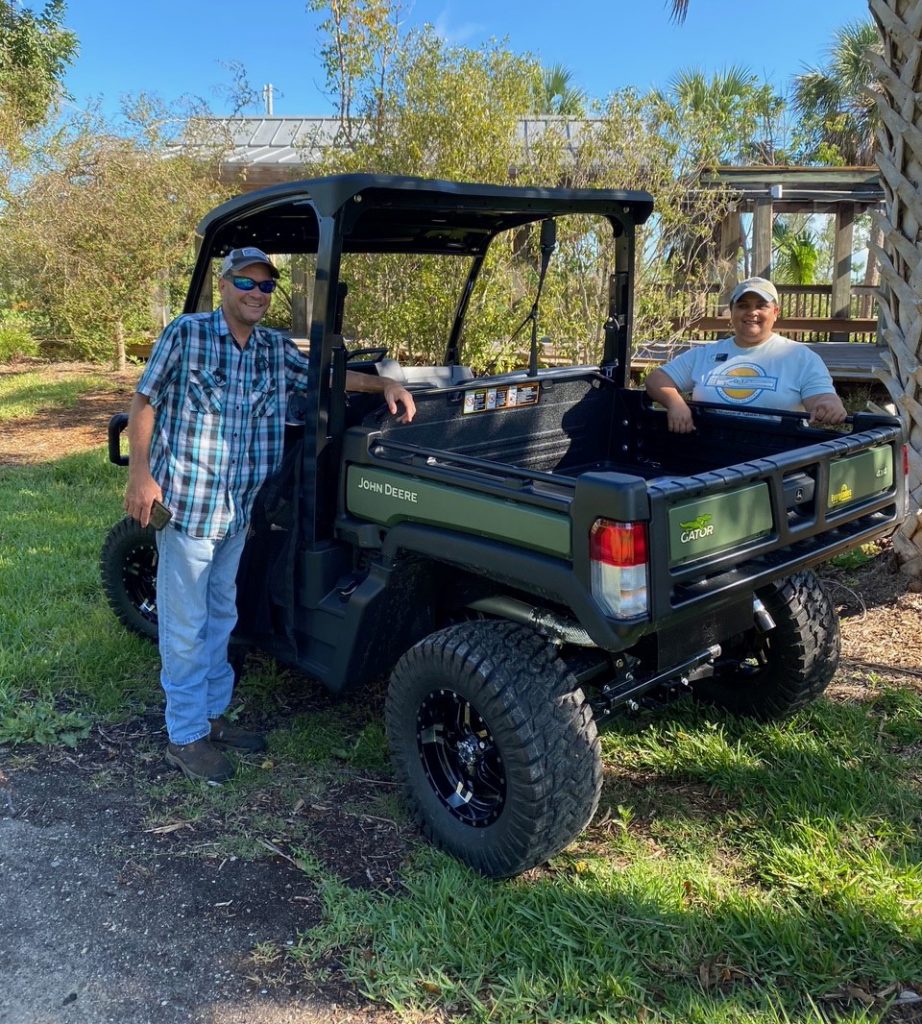Two people stand next to a John Deere Gator lightweight utility vehicle. They are looking at the camera and smiling