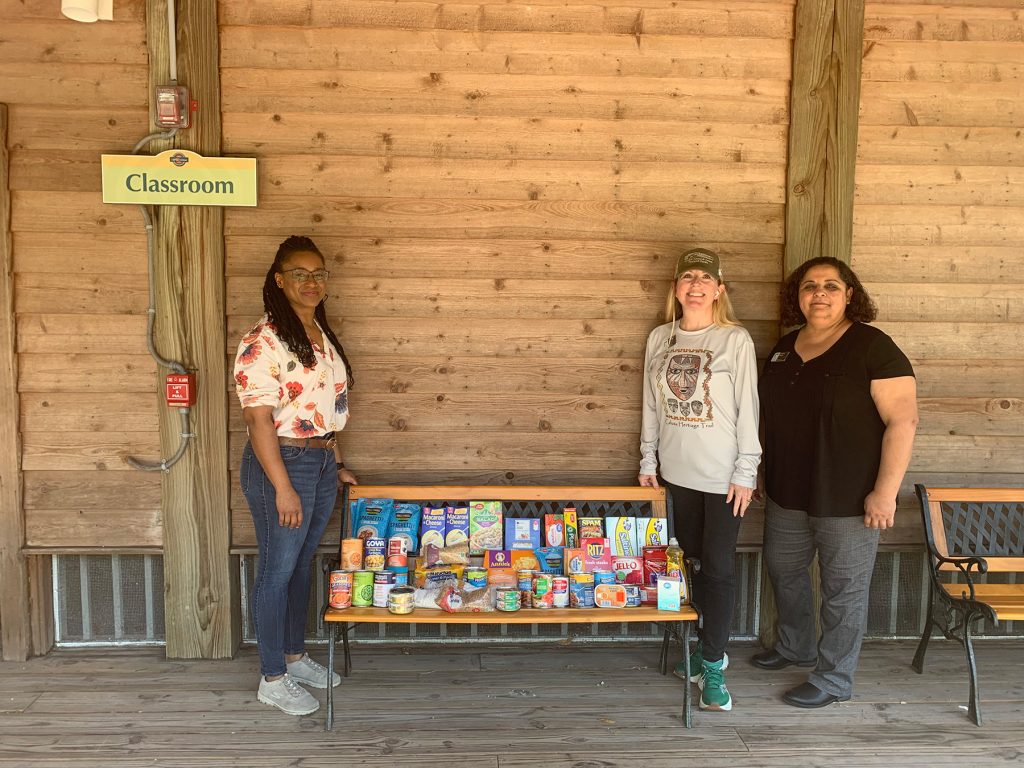 three people standing next to a bench filled with canned food