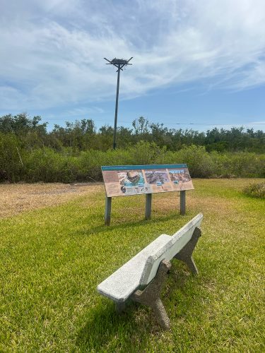 a bench set next to a sign along the Calusa Heritage Trail, a nesting platform with an osprey nest can be seen in the background
