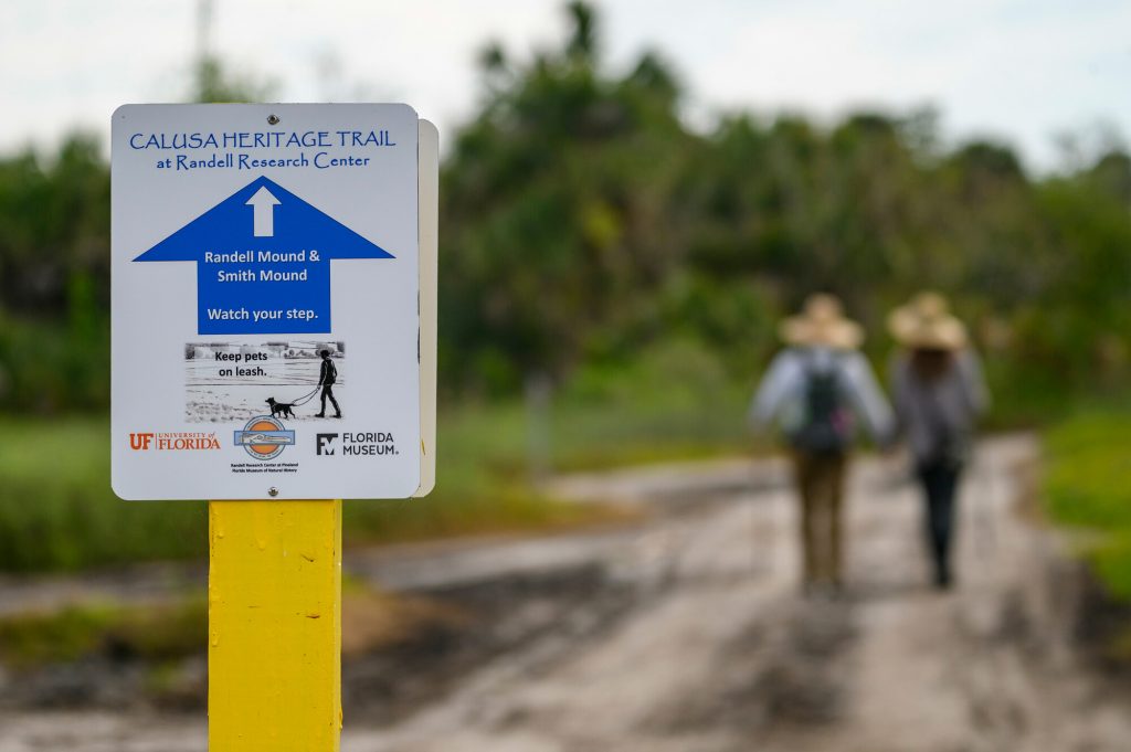 Directional sign to Randell Mound and Smith Mound set along the Calusa Heritage Trail at RRC. People are walking along the trail behind the sign.