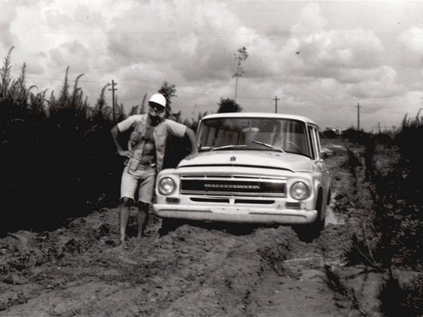 Crew member posing with a field truck that had become stuck in mud on the road, circa 1980s