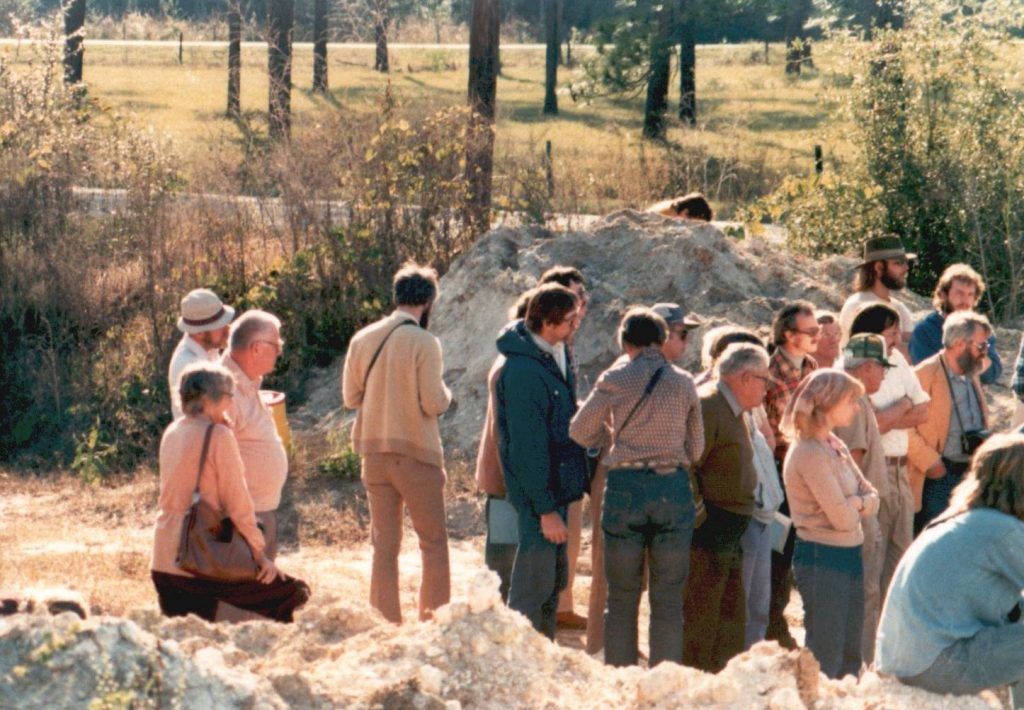 Group photo of about twenty people by sand piles, November 1980