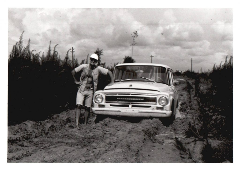Crew member posing with a field truck that had become stuck in mud on the road, circa 1980s