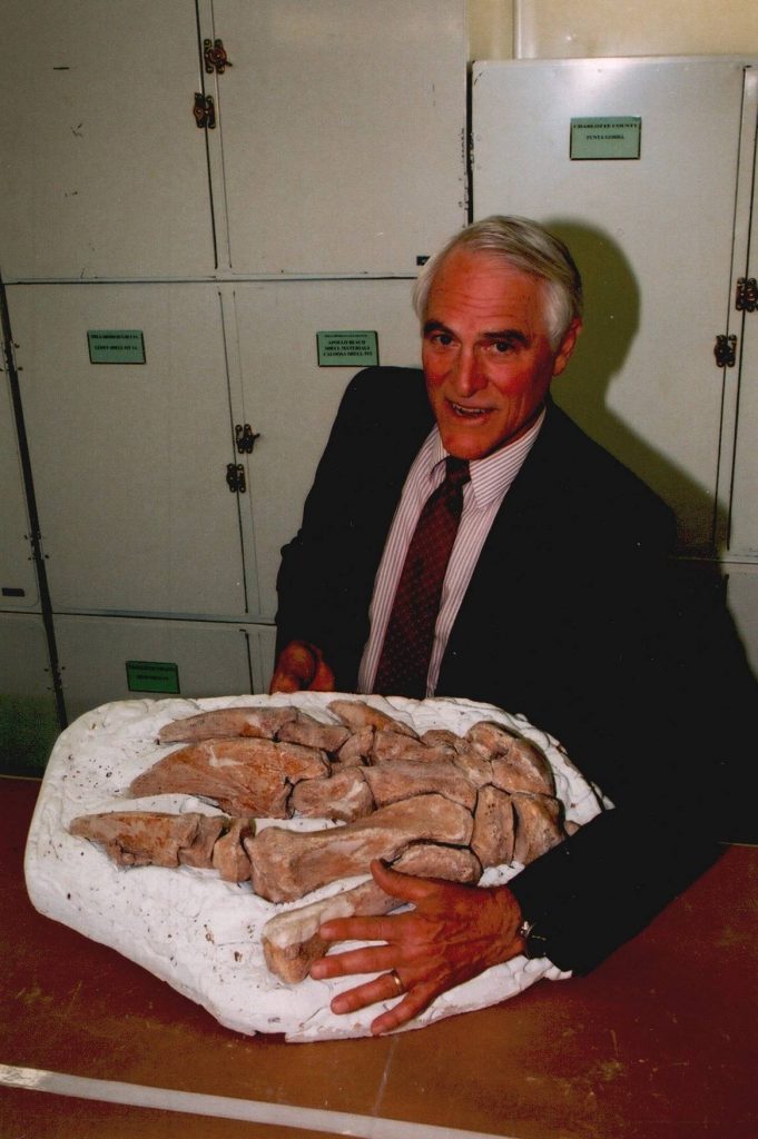 David Webb posing with his hand next to a reconstructed fossil sloth hand, March 20, 2000