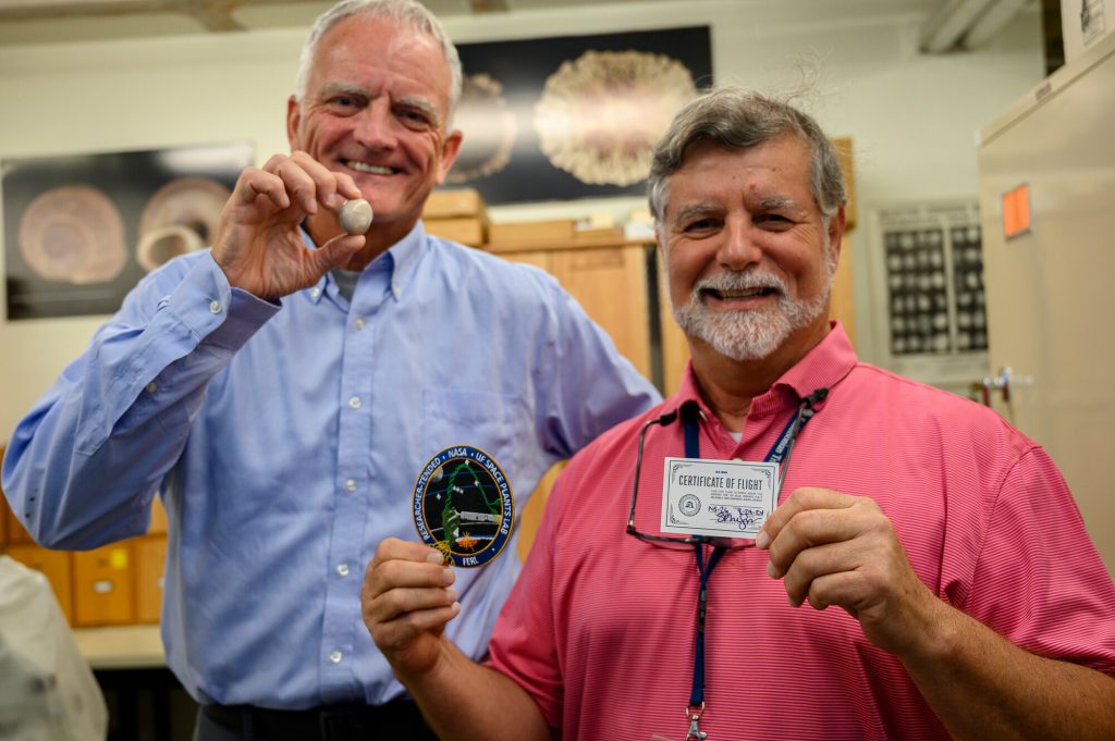 Two people holding at a patch and a certificate of flight and snail specimen