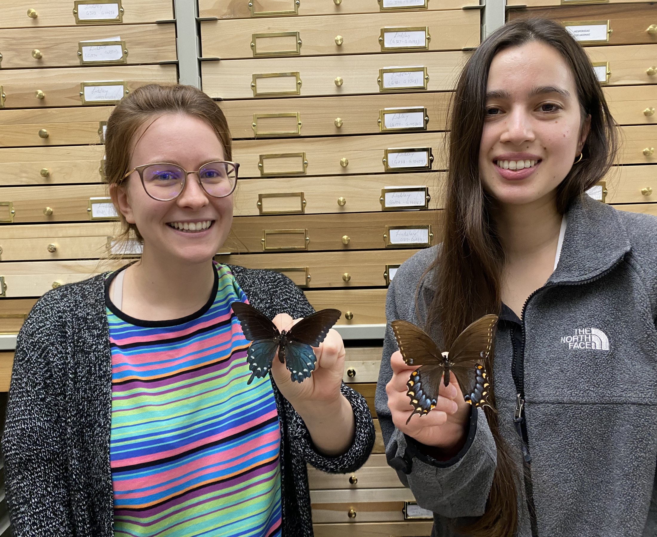 Picture of two women each holding a pinned specimen of a swallowtail butterfly.