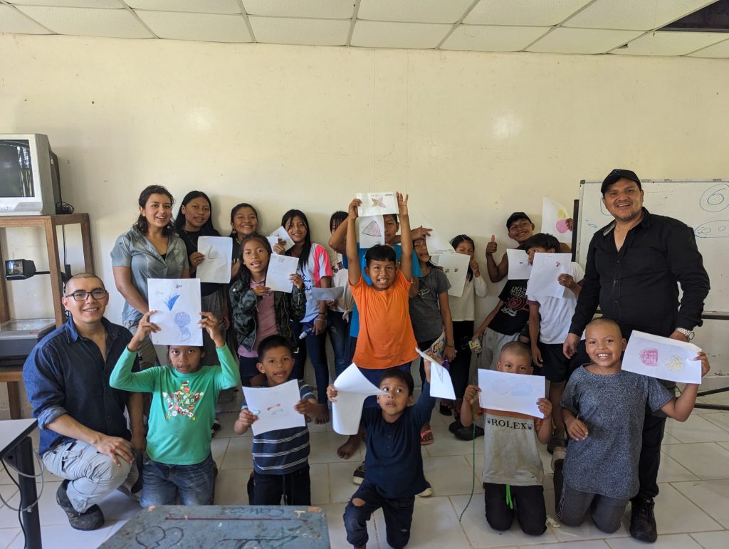 Picture of a group of children and teachers in Ecuador holding up drawings.