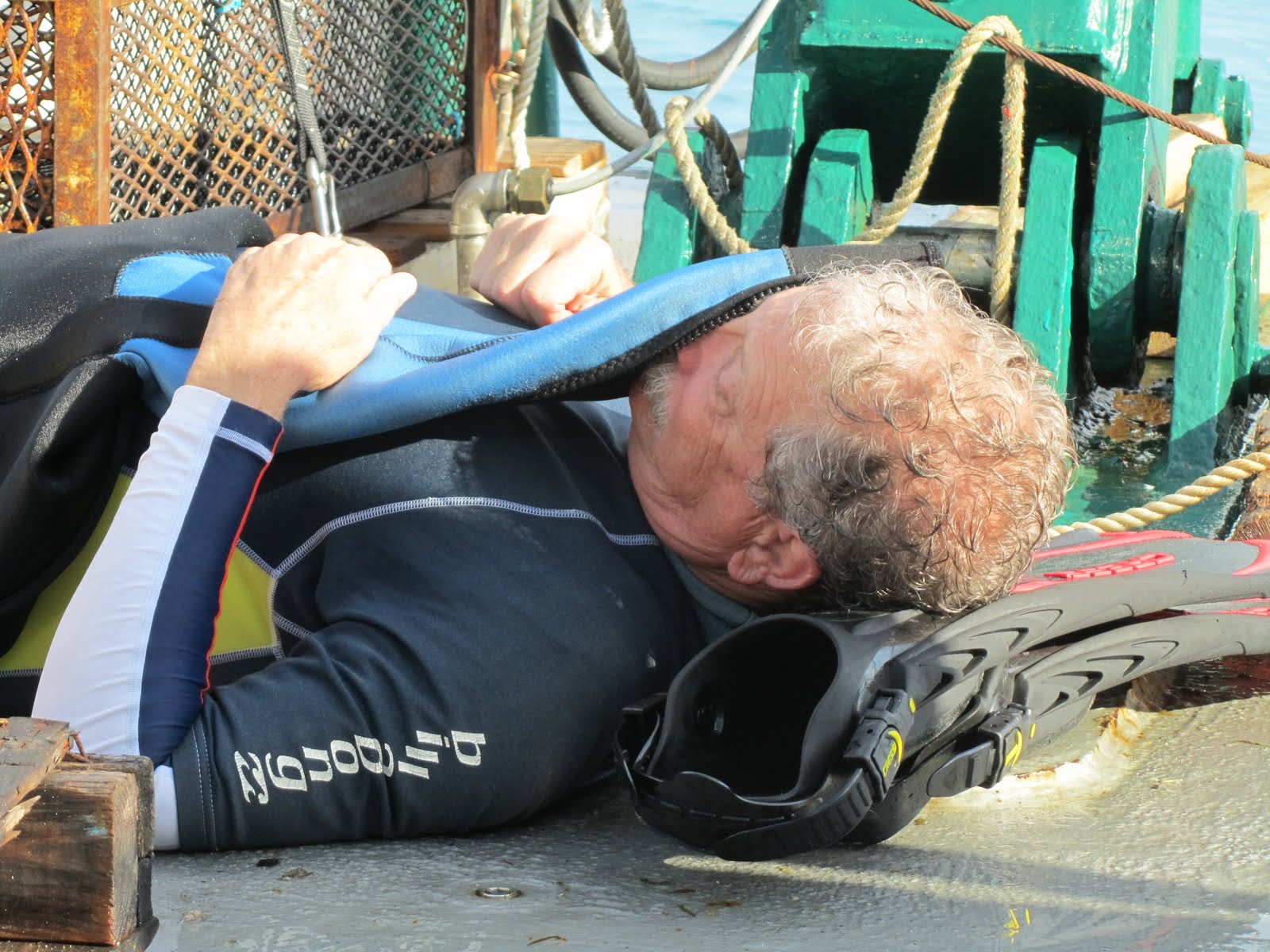 Jim napping on deck with his head on a pile of fins and a fin over his face