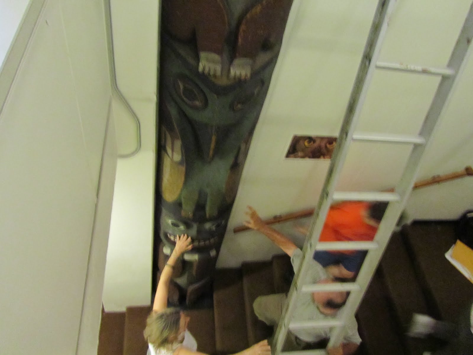 shot from above, museum staff finalizing the placement of the large totem pole in the stairwell