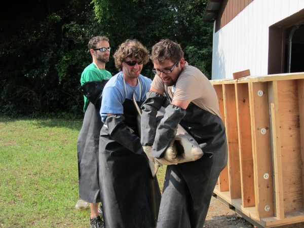 three men in black plastic aprons carrying a preserved shark