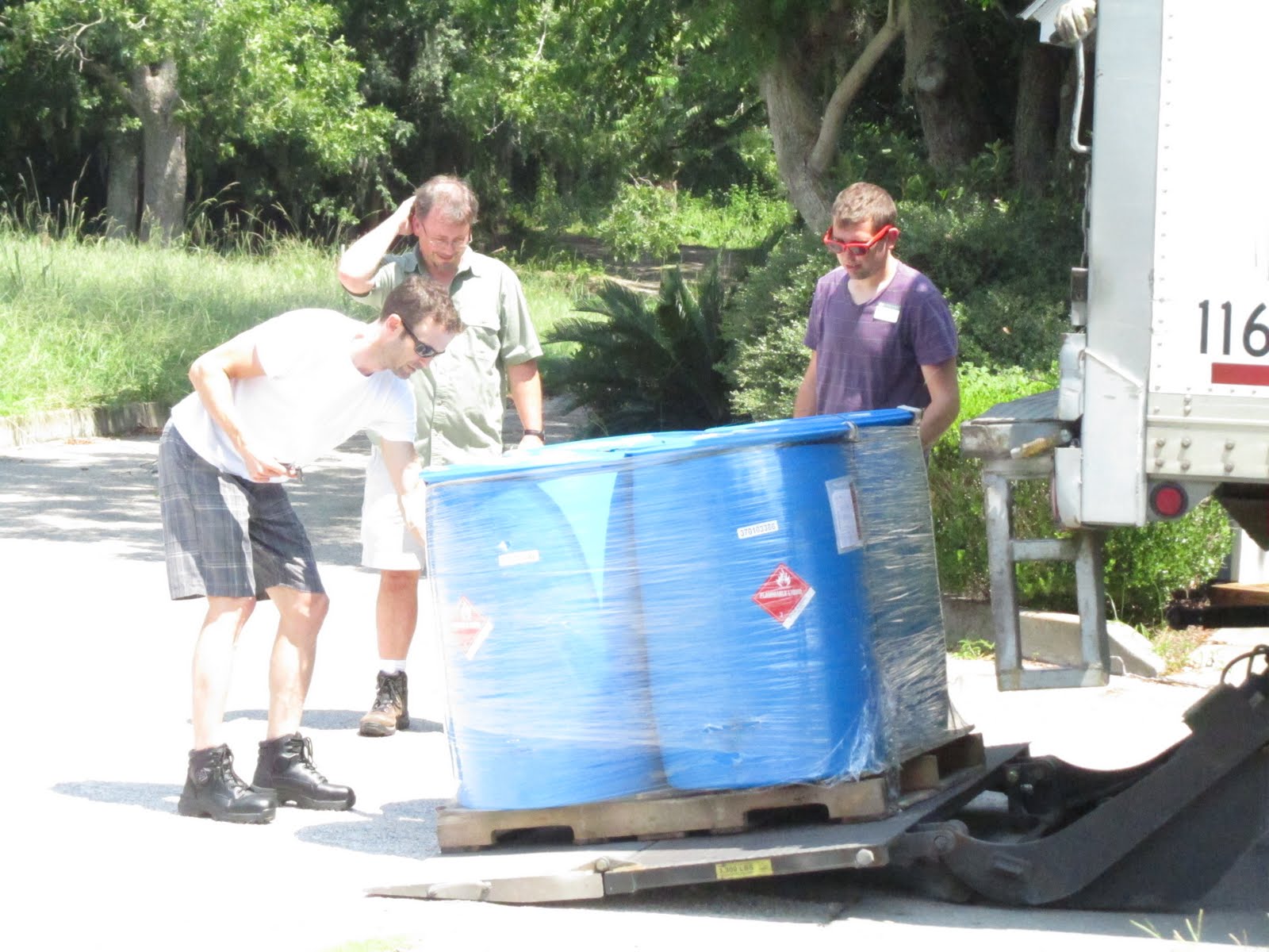 Rob, John, and Randy unloading 4 blue 55 gallon drums from a wooden pallet