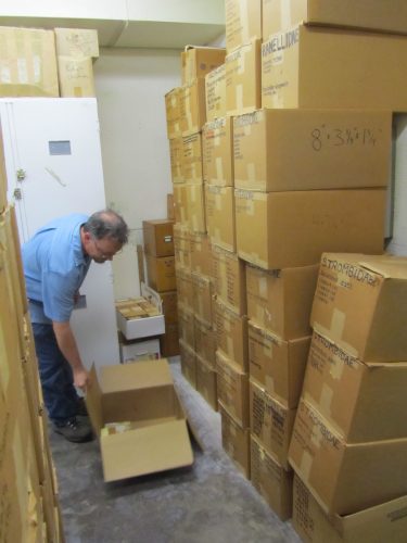 John in front of a wall of boxes checking the contents of a box on the floor