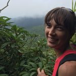 woman in pink/red tank top on the right of the frame looking back over her shoulder. cloudy rainforest stretching out past her