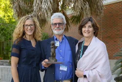 Man win trophy and two women smiling at camera