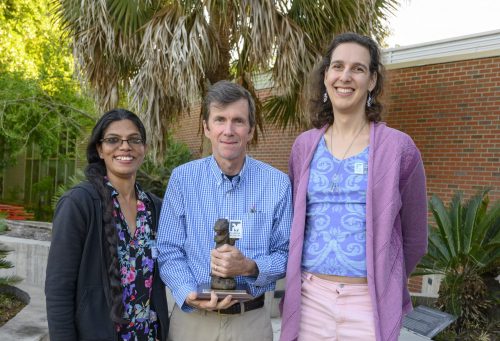 Man with trophy and two women smiling