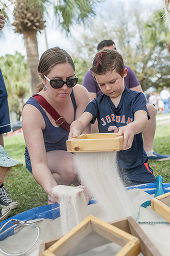 Woman helps child to sift through sand Visitors dig for fossils at ‘Can You Dig It?’