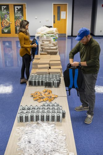 two people stand on either side of a table packing backpacks