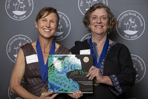 women wearing medals, smiling and holding a book